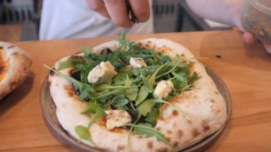 Şef pizzaya roka ve Dor küflü peynir koyar.