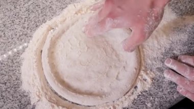 Mutfak çalışanı hamuru una batırılmış parmaklarıyla sarar.