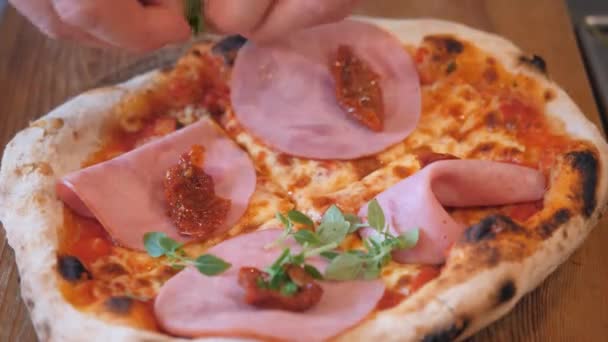 Hagelslag gescheurd arugula knijpen op gekookte pizza met ham — Stockvideo