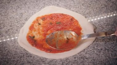 Pizzacı hamur parçasına ketçap sürüp kaşık sürüyor.