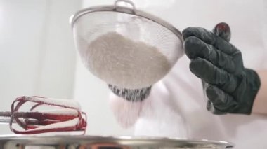 Fırıncı mutfakta süzgeçle un süzer.