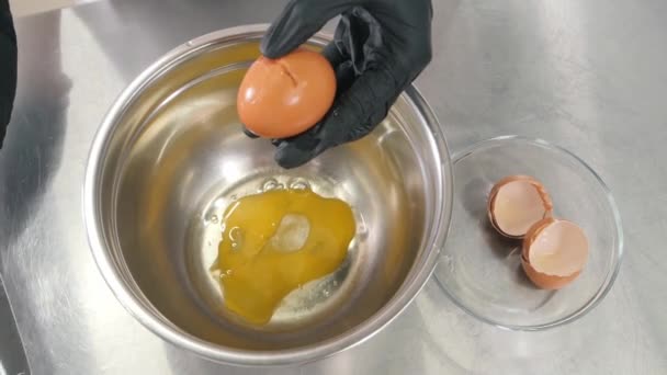 Kock bär handskar bryter ägg med kniv över metall skål — Stockvideo
