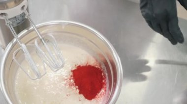 Fırıncı metal masadaki sıvı hamura kırmızı gıda renklendiricisi ekler