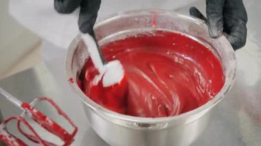 Şekerci kırmızı sıvı hamuru spatulayla karıştırıyor.