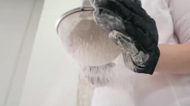 Çalışan mutfakta hamur yapmak için taze buğday unu süzüyor