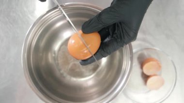 İnsan büyük metal kasenin üzerinde taze yumurtayı bıçakla kırar.
