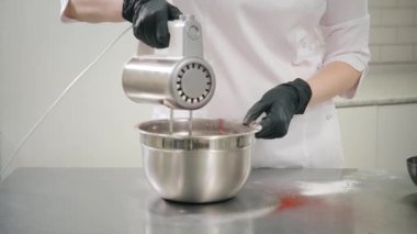 Şef hamur işini pişirmek için metal kaseye kırmızı sıvı hamur karıştırıyor.