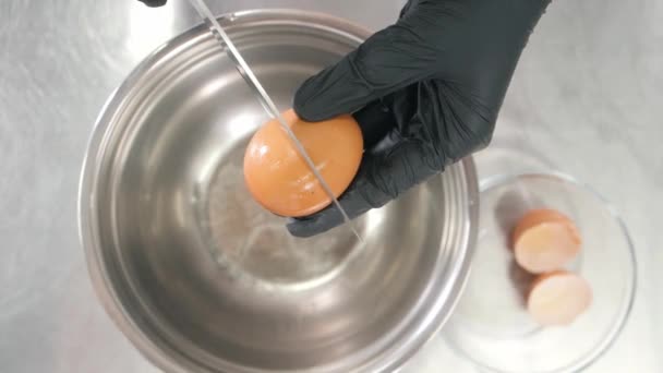 Osoba łamie świeże jajko nożem nad dużą metalową misą — Wideo stockowe