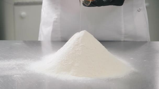 Baker in gloves adds egg to flour pile at table in kitchen — Stock Video