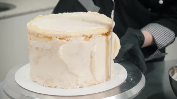 Confeiteiro em luvas pretas aplica nata doce no bolo — Vídeo de Stock