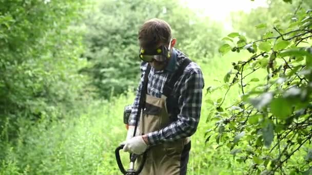 Mitarbeiter nimmt Schutzbrille ab und bleibt stehen, um Gras im Garten zu schneiden — Stockvideo