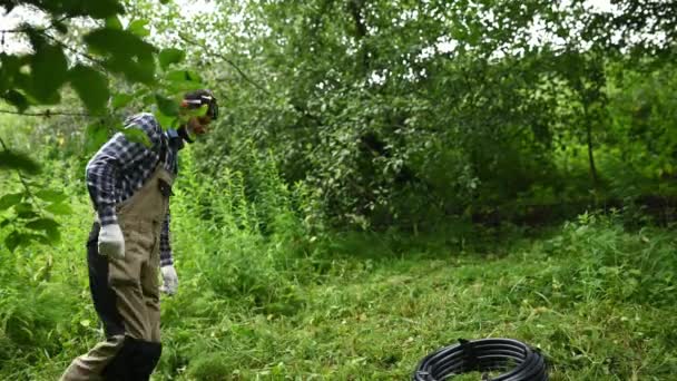 Zahradník přichází vzít svinutou černou hadici z trávníku v zahradě — Stock video