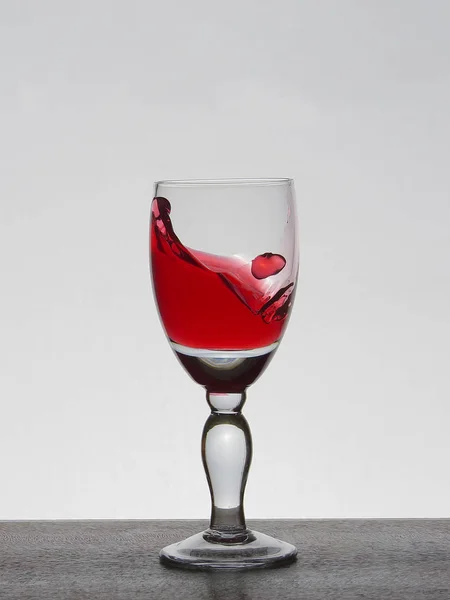 Rozpylać cieczy (czysta woda, czerwone wino) z czara szkła. — Zdjęcie stockowe