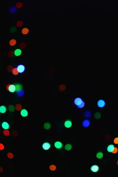 Gekleurde lichten (slinger) in het donker. Bokeh effect feestelijke verlichting. — Stockfoto