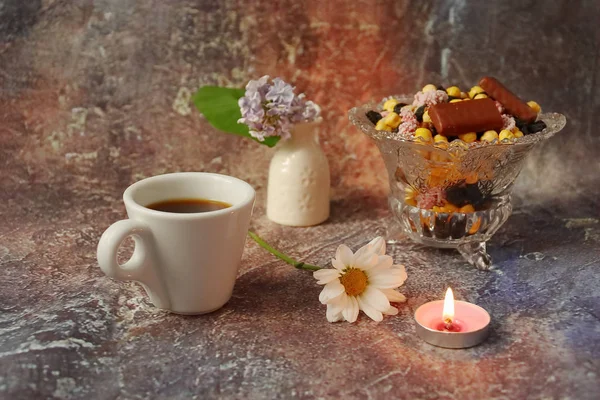 Morning coffee in a hurry: a cup of coffee, flowers in a vase, dried fruits and sweets in a vase, a burning candle.