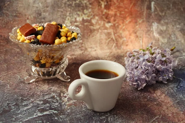 Cafeaua de dimineață în grabă: o ceașcă de cafea, flori într-o vază, fructe uscate și dulciuri într-o vază, o lumânare arzătoare . — Fotografie, imagine de stoc