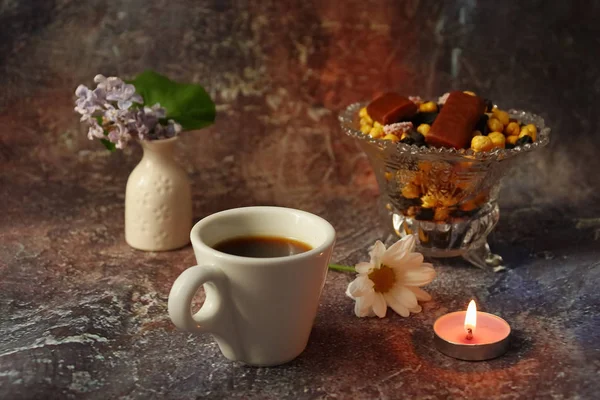 Morning coffee in a hurry: a cup of coffee, flowers in a vase, dried fruits and sweets in a vase, a burning candle.
