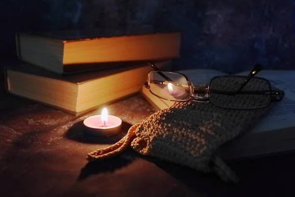 Lighted candles in an intimate setting, old books, yellowed from time to time, glasses in a knitted yellow thread. — Stock Photo, Image