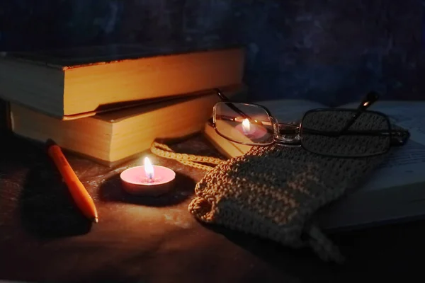 Lighted candles in an intimate setting, old books, yellowed from time to time, glasses in a knitted yellow thread. — Stock Photo, Image