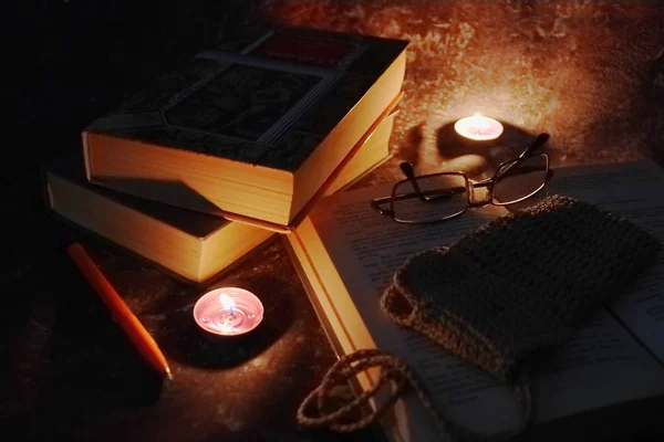 Lighted candles in an intimate setting, old books, yellowed from time to time, glasses in a knitted yellow thread. — Stock Photo, Image