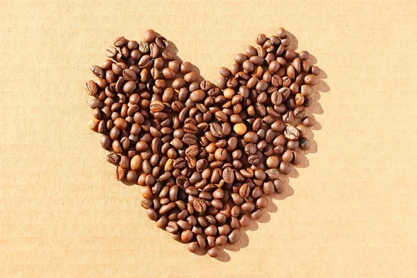 Spilled coffee. Grains of aromatic roasted coffee scattered in the form of a heart on a cardboard surface in the rays of the rising sun.