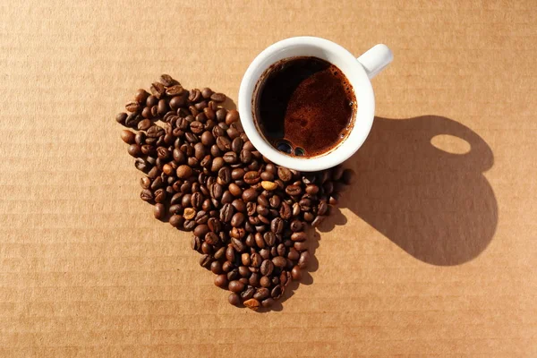 Un café derramado. Granos de café tostado aromático esparcidos en forma de corazón sobre una superficie de cartón en los rayos del sol naciente . — Foto de Stock