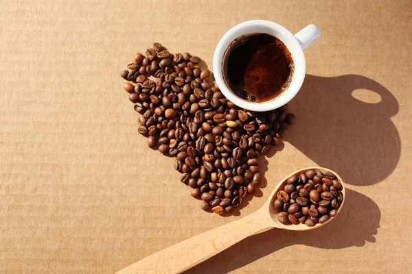 Spilled coffee. Grains of aromatic roasted coffee scattered in the form of a heart on a cardboard surface in the rays of the rising sun.