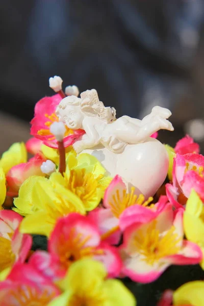 Anjo branco em um coração em um buquê de flores artificiais em um cesto . — Fotografia de Stock