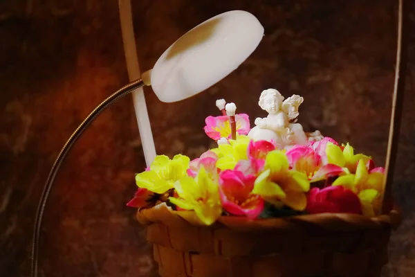 Anjo branco em um coração em um buquê de flores artificiais em um cesto . — Fotografia de Stock