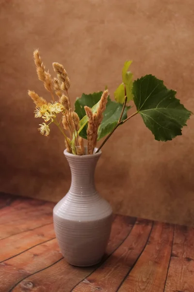 Jarrón blanco con un ramo de flores amarillas fragantes y hojas de tilo y erizos de hierba seca . — Foto de Stock