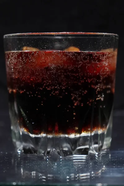 Un verre fumant de boisson rouge-marron apaisante et froide avec des glaçons . — Photo