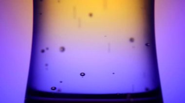 Sarı-mavi bir arka plan üzerinde soğuk köpüklü maden suyu ile sisli bir cam. Gaz kabarcıkları yükselir.