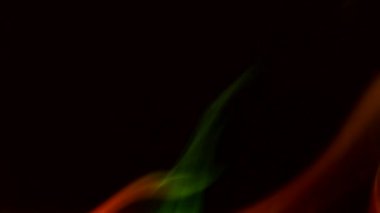 Karanlık bir zemin üzerinde kıvrımlı duman kabarcıkları, farklı renklerde ışık tarafından aydınlatılıyor..