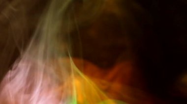 Karanlık bir zemin üzerinde kıvrımlı duman kabarcıkları, farklı renklerde ışık tarafından aydınlatılıyor..