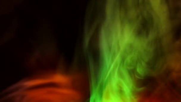 Kudrnaté plíživé obláčky kouře na tmavém pozadí, osvětlené světlem různých barev. — Stock video