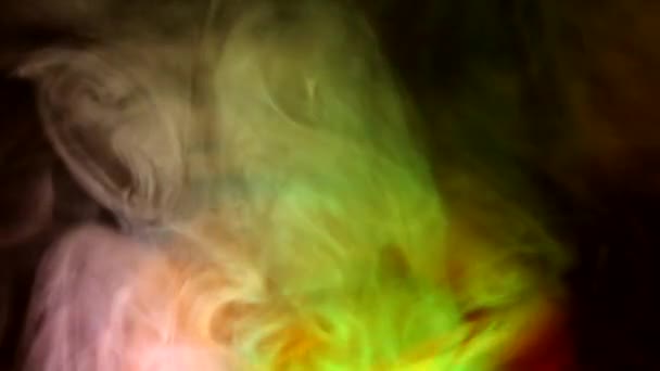 Lockigt krypande puffar av rök på en mörk bakgrund, upplyst av ljus med olika färger. — Stockvideo