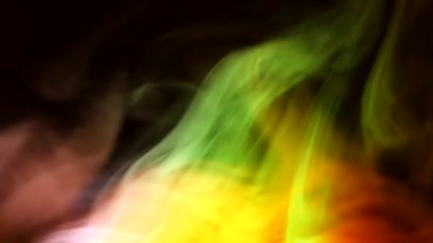 Κέρλι σέρνεται ξεφλούδισμα του καπνού σε ένα σκοτεινό φόντο, φωτίζεται από το φως με διαφορετικά χρώματα. — Αρχείο Βίντεο