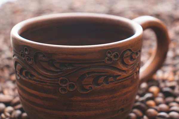 Brown ceramic cup with painted patterns. Coffee cup on the table. Empty cup in scattered coffee beans.