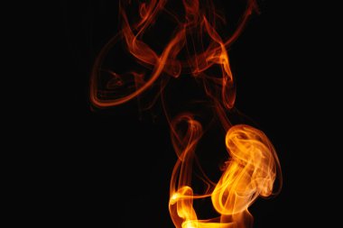 Siyah arka planda turuncu duman. Renkli duman. Duman turuncu ışıkla aydınlatılıyor. Tuhaf heceleyici alevler.