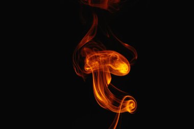 Siyah arka planda turuncu duman. Renkli duman. Duman turuncu ışıkla aydınlatılıyor. Tuhaf heceleyici alevler.