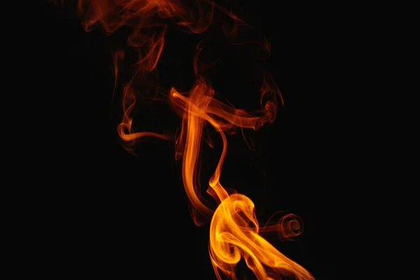 Orange smoke on a black background. Colored smoke. Smoke illuminated by orange light. Bizarre spellbinding flames.