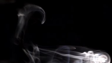 Yanan bir tütsü çubuğundan çıkan duman. Karanlık bir arka planda tuhaf bukleler.