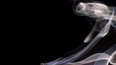 Yanan bir tütsü çubuğundan çıkan duman. Karanlık bir arka planda tuhaf bukleler.