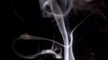 Yanan bir tütsü çubuğundan çıkan duman. Karanlık bir arka planda tuhaf bukleler.