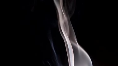 Yanan bir tütsü çubuğundan çıkan duman. Karanlık bir arka planda tuhaf bukleler.