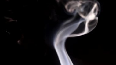 Yanan bir tütsü çubuğundan çıkan duman. Karanlık bir arka planda tuhaf bukleler.