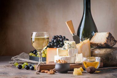 various types of cheese with honey, grapes and wine on rustic background clipart