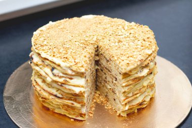 Kremalı katmanlı pasta, siyah bir masanın üzerine kırıntılar serpiştirilmiş. Pastanın bir parçası kesildi bile.