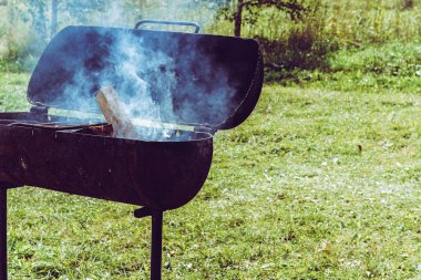 Güneşli yaz arka planda yangın ve duman ile metal mangal. Paslı bir ızgara üzerinde bir şiş Barbekü için odun kömür hazırlanması.