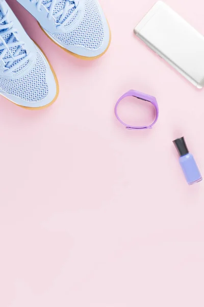 Woman sneakers, fitness tracker and smartphone on pastel pink background. Sport fashion concept. Flat lay